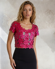 Woman wearing a pink floral top and black skirt against a textured wall.